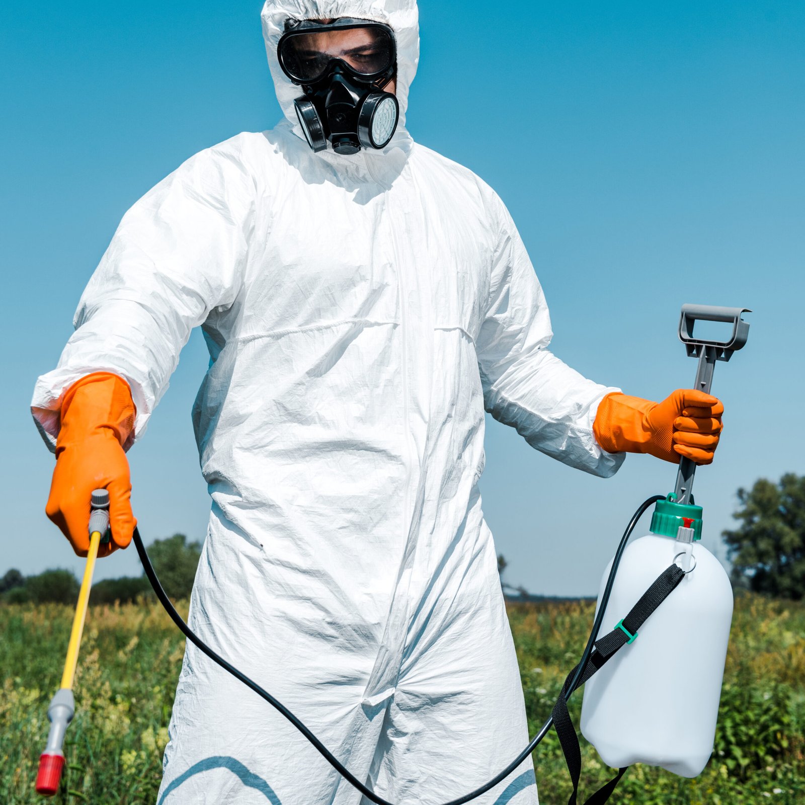 exterminator in orange latex gloves and white uniform holding spray outside exterminator in orange latex gloves and white uniform holding spray outside